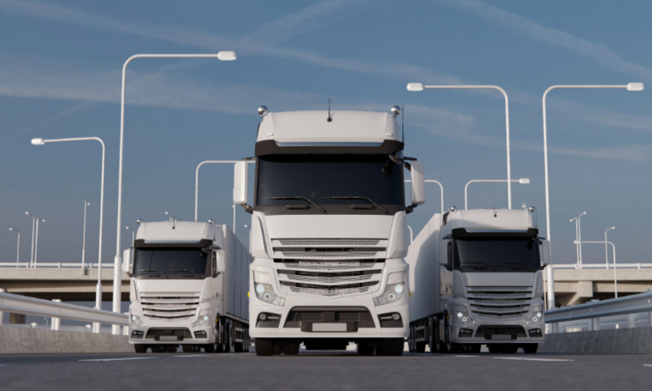 A fleet of modern heavy-duty trucks driving on a highway under clear skies.